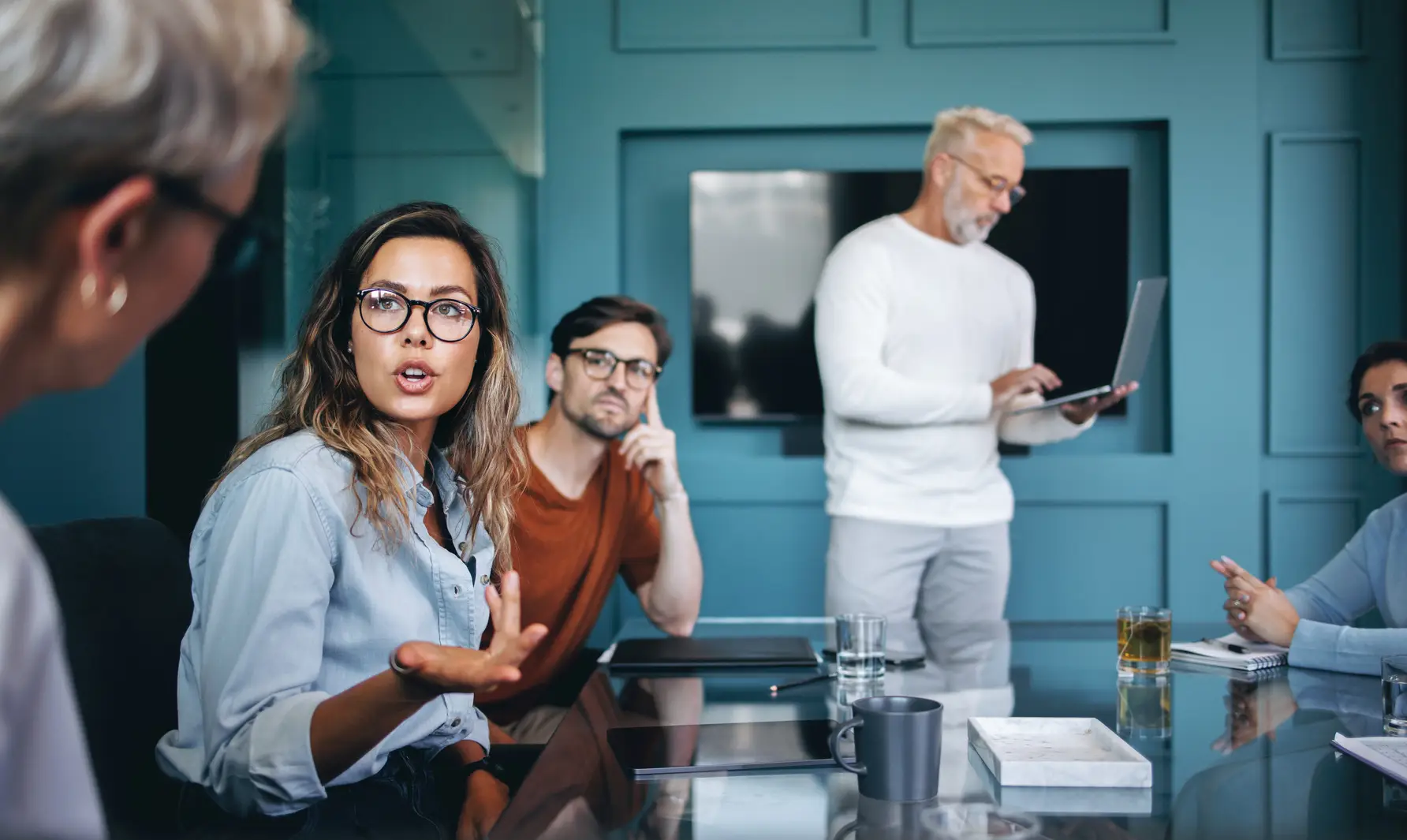Young female professional discussing innovative ideas with her colleagues in a meeting. Business woman actively collaborating with her team in a corporate boardroom setting.