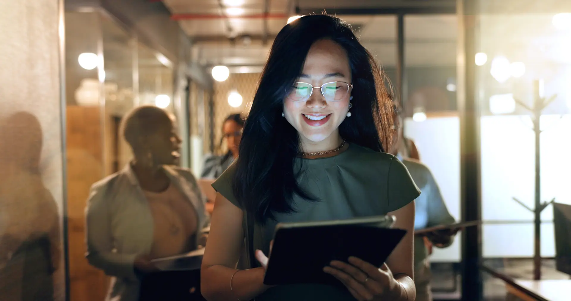 Night, tablet and business people walking in office after finishing work task. Tech, overtime and Asian woman with group of friends going home after working late on sales project in dark workplace